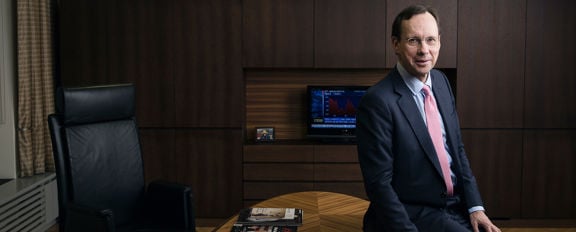 The Group CEO Kari Stadigh sitting casually, leaning against the edge of the office desk.